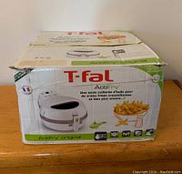 T-fal Actifry air fryer in original white box with green accents. Box is worn and torn at edges but label and branding visible.
