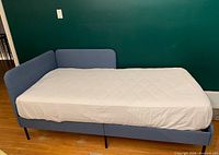 Front-on view of blue fabric daybed with white fitted sheet.