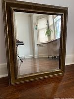 Front view of a brown wood framed rectangular mirror reflecting a room with hardwood floor and window.