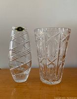 Two crystal cut glass vases placed on wooden surface, showing both sizes and designs