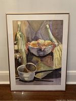 Full view of the framed still-life watercolour painting showing bottles, a bowl with fruit, cups, and a knife.