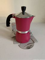 Front and side view of the fuchsia Bialetti 3-cup espresso maker with black handle and knob, silver band, and Bialetti logo.