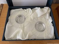 Two glass candle holders with metal centers placed in a padded presentation box.