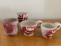 All four handmade pottery cups arranged on a wooden table, showing two with handles and two without.