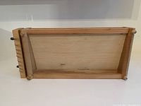 Photo of rectangular wooden pasta chitarra frame showing front surface with tightly strung metal wires and smooth wooden base with slanted board for pasta to slide off.