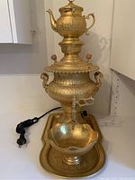 Full view of large gold electric samovar with teapot on top, caviar dish, and serving tray underneath. Includes European plug and cord.