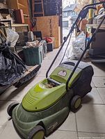 Full view of green Sun Joe MJ401E lawn mower with handle and rear grass collection bag in garage setting.