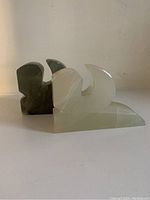 Pair of onyx stone bookends, one dark green and one translucent white, with carved abstract shapes angled side view.