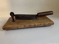 Image of the antique pioneer tool showing wooden base with mounted metal blade and pivoting mechanism, blade positioned down.