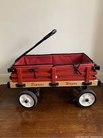 Side view showing wooden red panels, black metal supports, white-rimmed wheels, and handle in upward position.