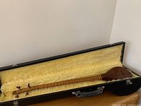 Full view of Setar inside open protective case showing plush yellow interior and wooden instrument body with neck and headstock.