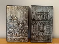 Two pewter relief plaques with architectural designs mounted on wood, showing the front details.
