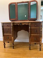 Full front view of the solid wood vanity showing six drawers, turned legs, and triple mirror attached on top.
