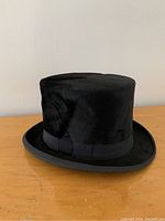 Profile view of black fur felt top hat with grosgrain ribbon band and rolled brim