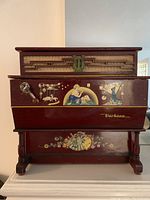 Front view showing red wood, painted floral and figure details, crank handle on left.