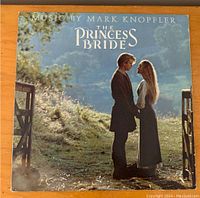 Front cover photo of The Princess Bride vinyl record showing a man and woman in period costume standing outdoors between open gates, with text 'Music by Mark Knopfler - The Princess Bride'.