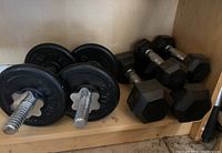 Photo of two adjustable dumbbells with chrome threaded handles and black cast iron weight plates on a shelf.