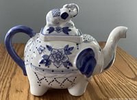 Side view of the blue and white ceramic elephant teapot showing painted floral details, blue handle, and elephant lid.