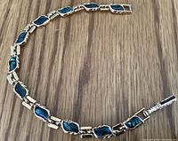 Full view of gold tone bracelet with green abalone marquise-shaped links laid flat on wood surface.