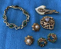 Mixed lot of jewelry on blue fabric including bracelet, brooches, clip-on Christmas earrings.