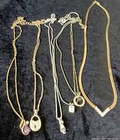 Overview of six necklaces laid out, displaying various pendant styles and chain types on black fabric.