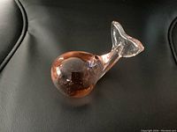 Front side view of pink glass whale-shaped paperweight showing bubbles inside glass body and clear tail fin.