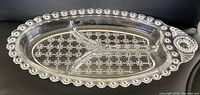 Side angle view of the clear glass divided pickle dish with jewel pattern and scalloped rim, highlighting one end with decorative handle.