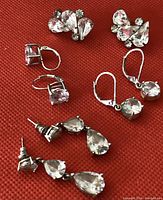 Four pairs of pierced earrings displayed on red fabric, showing various styles including lever back and stud backs, some with clear crystals.