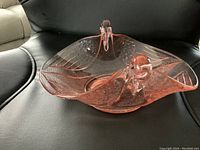 Pink depression glass candy dish shaped like two swans, with etched wing details, viewed from an angle showing one swan's side profile and the overall dish shape.