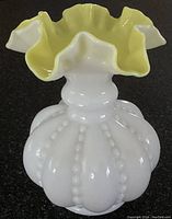 Front view of vintage white Fenton vase with yellow ruffled top and beaded body detail.