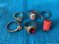 Top view of six ladies rings on blue fabric showing stone details and band styles