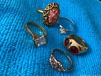 Close view of the five assorted rings on blue fabric background showing various stones and metal tones.