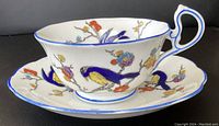 Side view of teacup and saucer showing colorful bird and floral hand-painted style design on white porcelain with blue rim and handle accents.