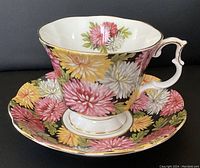 View of teacup and saucer showing floral pattern with pink and yellow flowers on black background and gold trims