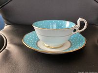 Side view of blue polka dot Royal Albert teacup stacked in center of matching saucer, showing the handle and gold rim detail.