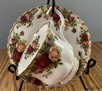 Photo showing the teacup hanging on the matching saucer, both with floral rose designs and gold scalloped edges.