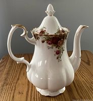 Front left angle view showing the teapot body, handle with gold trim, floral pattern, and lid finial.