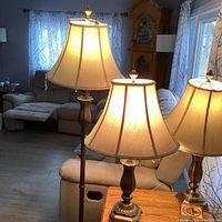 Photo showing two table lamps with pewter-like bases and beige fabric shades on a wooden surface in living room.