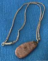 Full view of silver chain with stone pendant lying on blue fabric, showing chain length and pendant size.