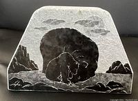 Clear image of the soap stone napkin holder showing the black etched bear design in a natural mountainous background with clouds.