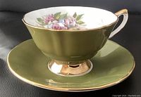 Side view of the olive green teacup on matching saucer showing gold trim and floral interior