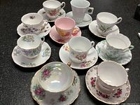 Top-down view of 10 floral and patterned teacups with matching saucers on a black surface.