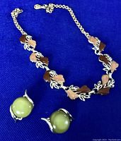 Choker necklace and green clip-on earrings laid on blue fabric, showing the leaf and petal design of the necklace and the rounded green earrings