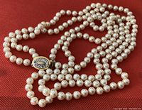 Close-up photo of vintage double strand pearl necklace showing pearls and gold-tone oval clasp with small stones.