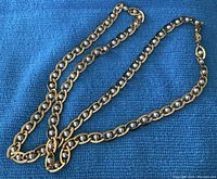 Full view of a vintage gold-tone link chain necklace laid flat on a blue textured cloth background, showcasing faux pearl beads integrated in the links, measuring approximately 28 inches.