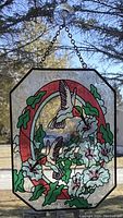 Front view of stained glass window hanging featuring hummingbirds in flight surrounded by flowers and leaves, hung on window by chain and suction cup.
