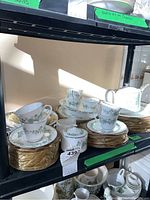 Stacks of plates, cups and saucers on shelf showing dinner, salad and bread plates with teacups and saucers.
