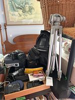 Overview of box containing multiple cameras, a large tripod, black backpack, cases and pouches