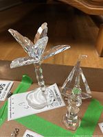 Clear crystal Swarovski palm tree, sailboat, and lighthouse figurines displayed on a brown surface with green tape.