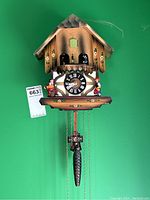 Front view of chalet-style wooden cuckoo clock showing dial, dancers, figurines and pinecone weights